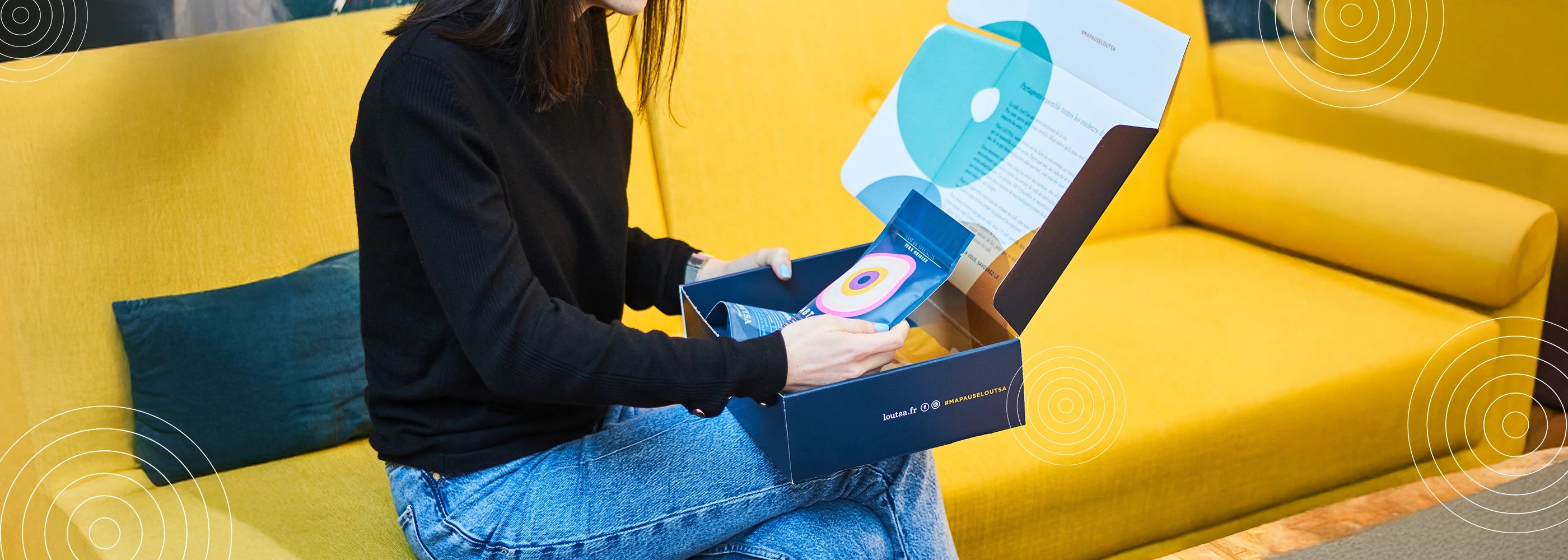 Femme assise sur un canapé jaune ouvrant une box café Loutsa contenant un sachet de café de spécialité coloré, dans le cadre d’un abonnement.