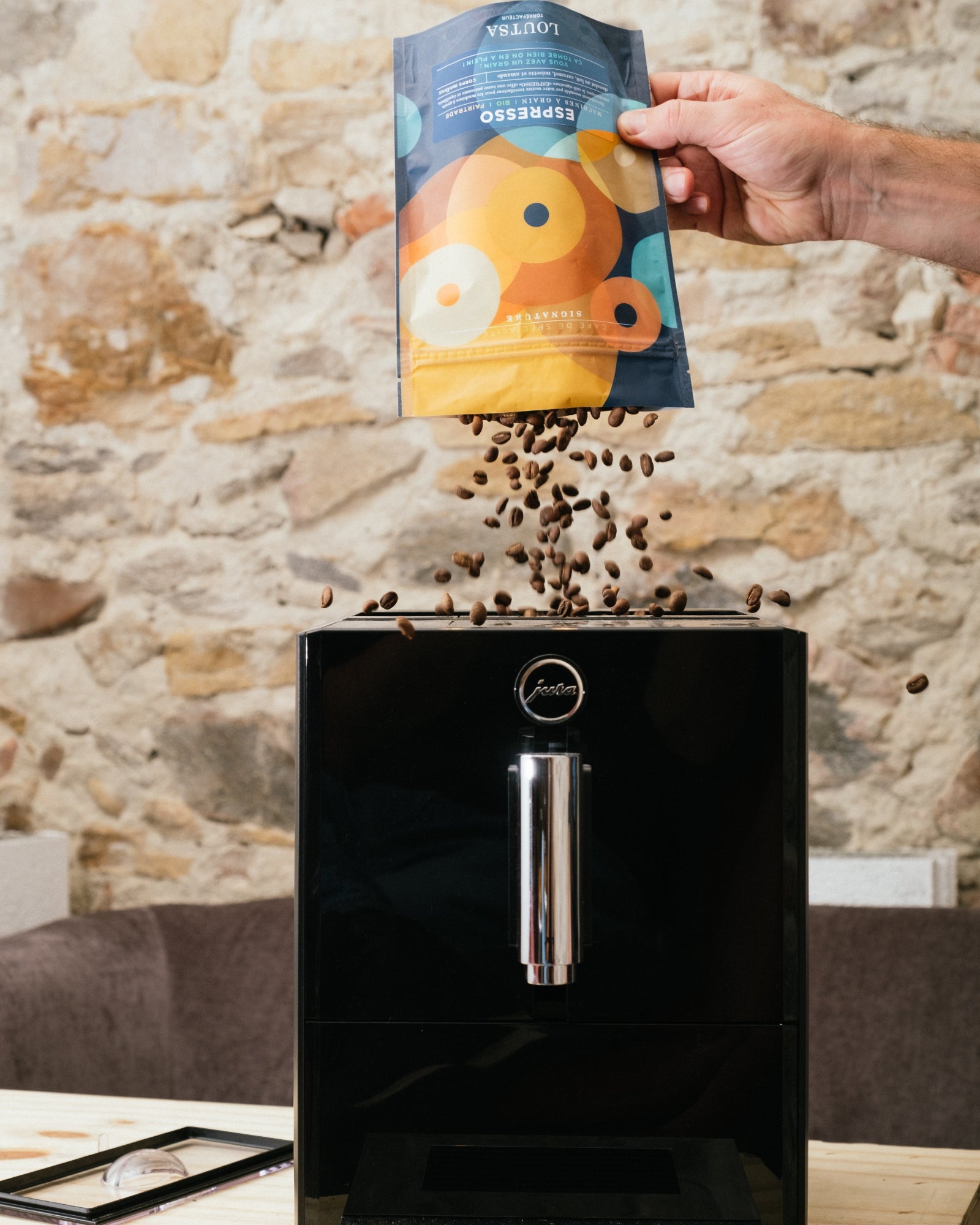 main tenant un sachet de café ESPRESSO LOUTSA, versé dans une machine à café automatique JURA