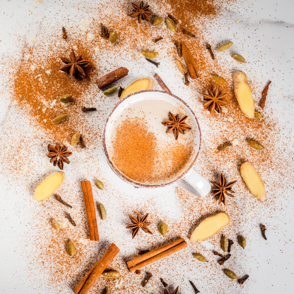 Une tasse de chai vue de dessus, saupoudrée de cannelle et entourée d'épices