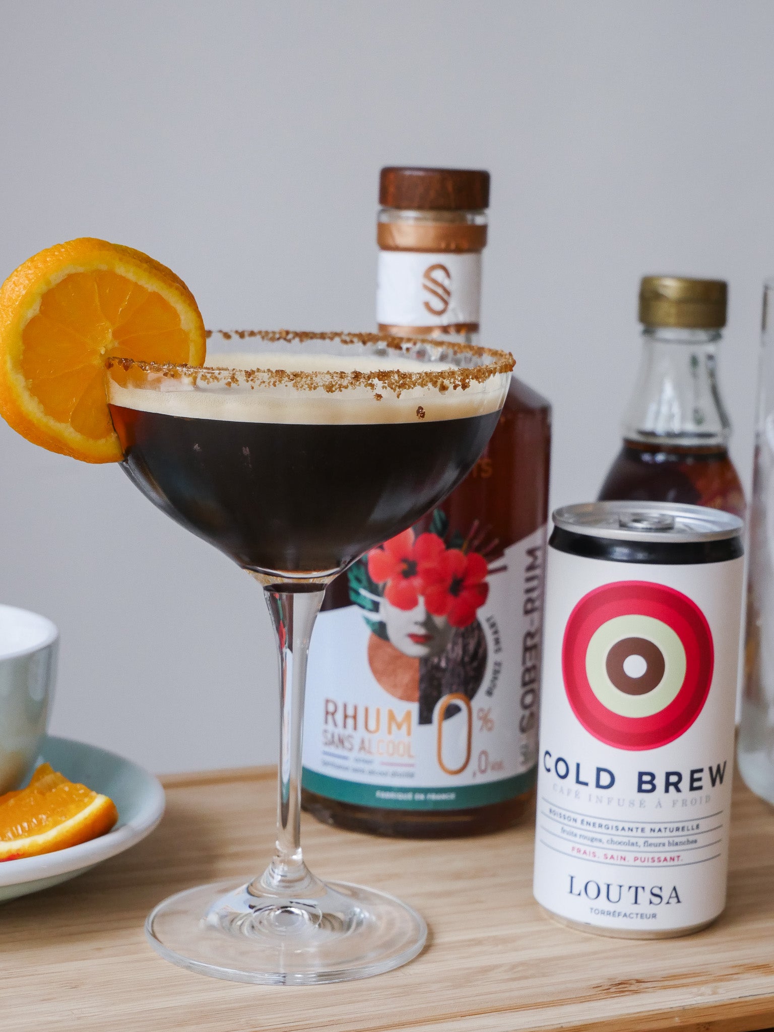 cocktail à base de café dans un verre à pied surmonté d'une tranche d'orange, en fond une bouteille de cold brew et une bouteille de rhum