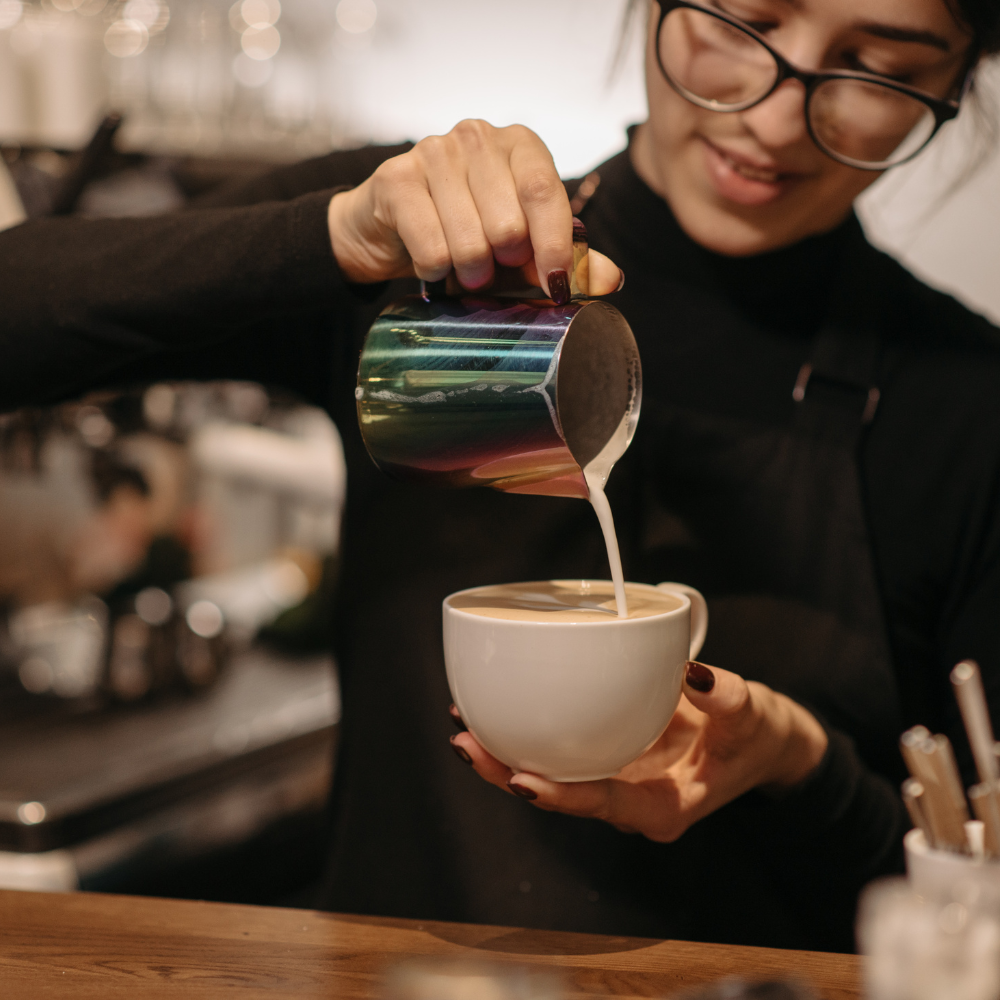 Une barista réalisant un latte art dans une tasse blanche