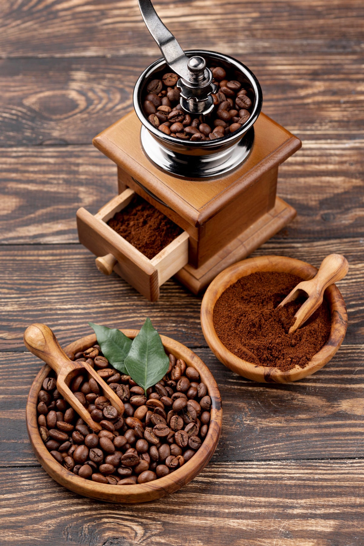 sur une table en bois, vu de dessus un moulin à café, un bol avec du café moulu et un bol avec du café en grain