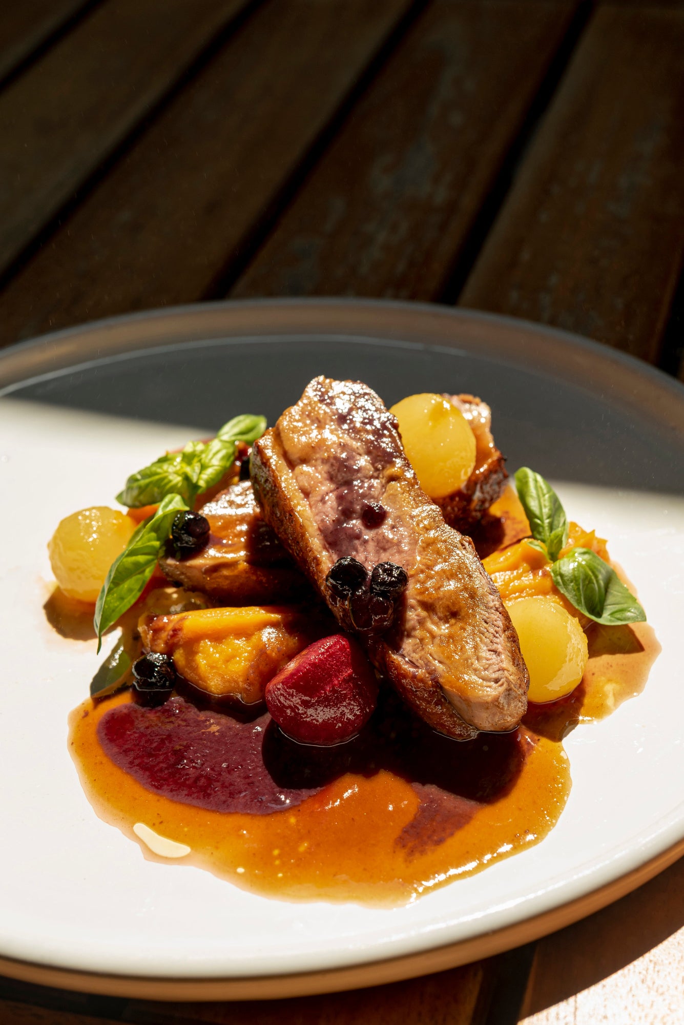 assiette blanche dressée avec un magret de canard infusé au café, ses légumes et quelques olives et brins de basilic