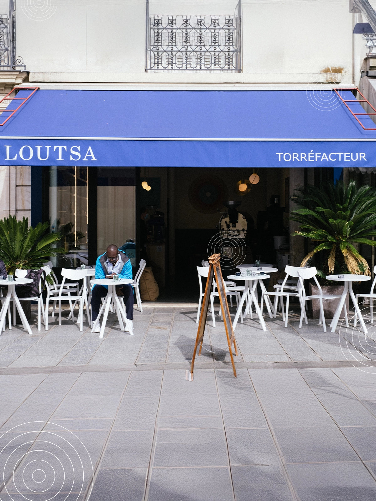 Devanture de la boutique de torréfaction Loutsa, avec terrasse et client assis en extérieur à une table blanche, sous un auvent bleu.