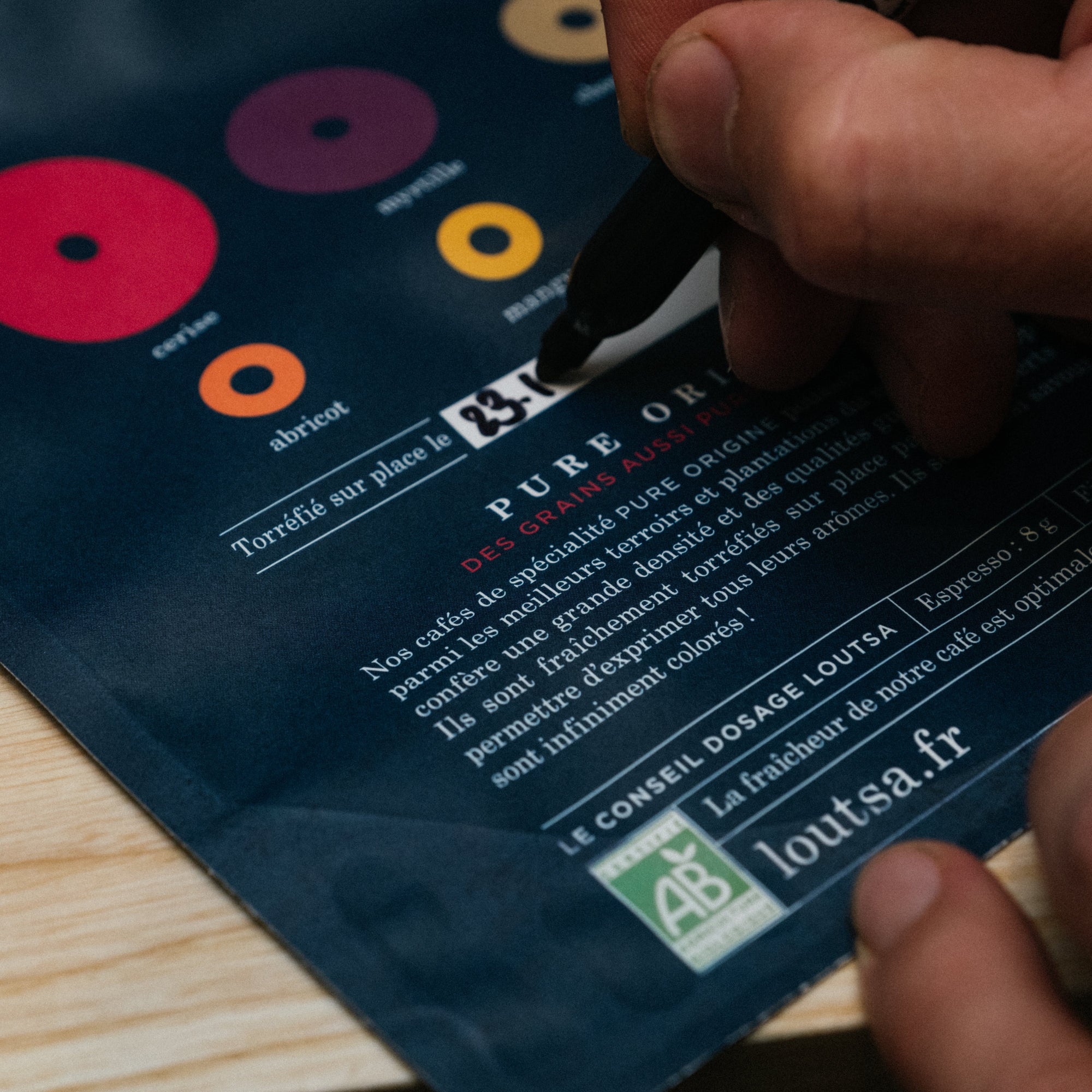 sachet de café vide sur lequel une main écrit la date de torréfaction au marqueur noir